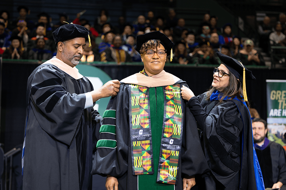 Reginald Silver, Belk College’s associate dean of graduate programs and executive education (left) and Pinku Mukherjee, interim associate provost and dean of the Graduate School (right) hooding DBA graduate Denise Wynn.