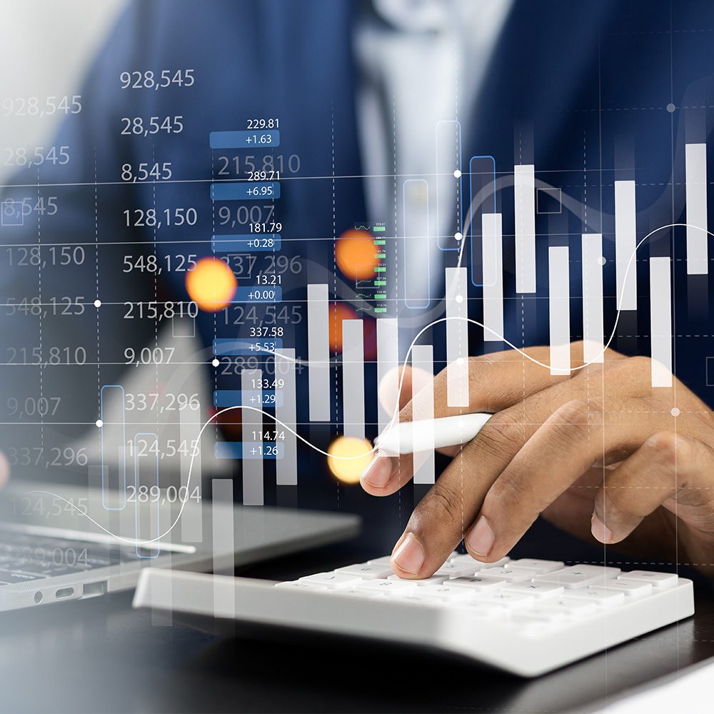 Undergraduate programs in finance, finance and accounting concentration. Person sitting at a desk with a laptop and calculator. A mixed spreadsheet and chart are projected in front of their hands. 