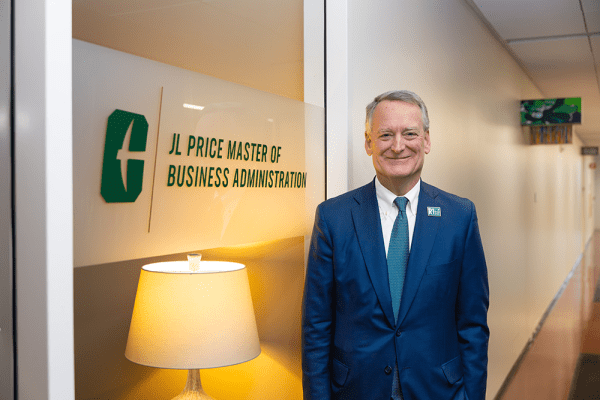 Joe L. Price '83 stands before a glass window in the Dubois Center that bears a logo of the newly named JL Price MBA