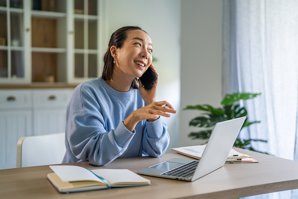 young woman on the telephone while working from home with a laptop, notes and files